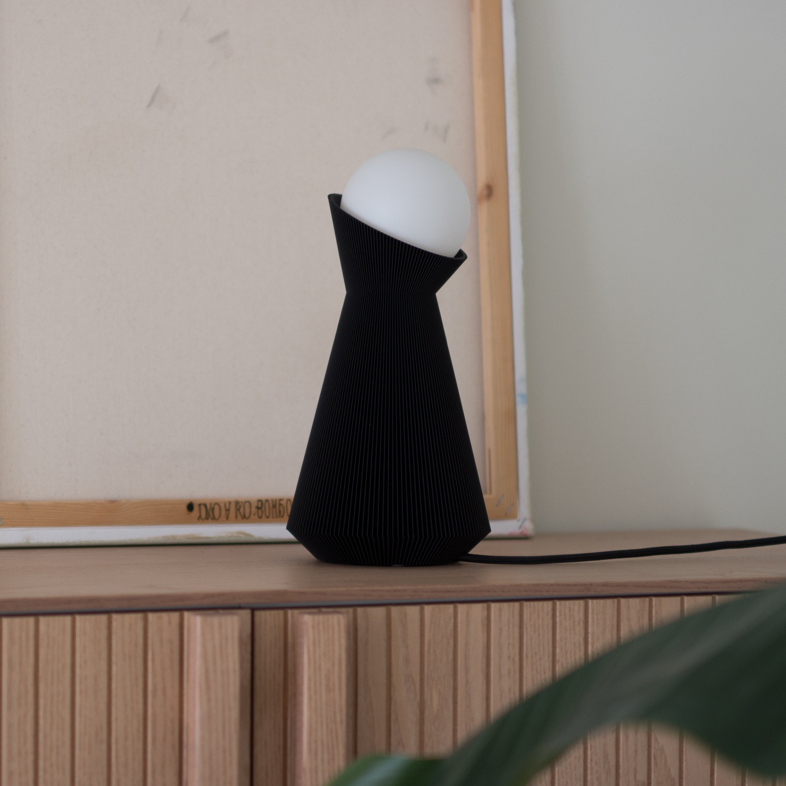 Black lamp with white bulb on a wooden surface next to an empty wooden frame.