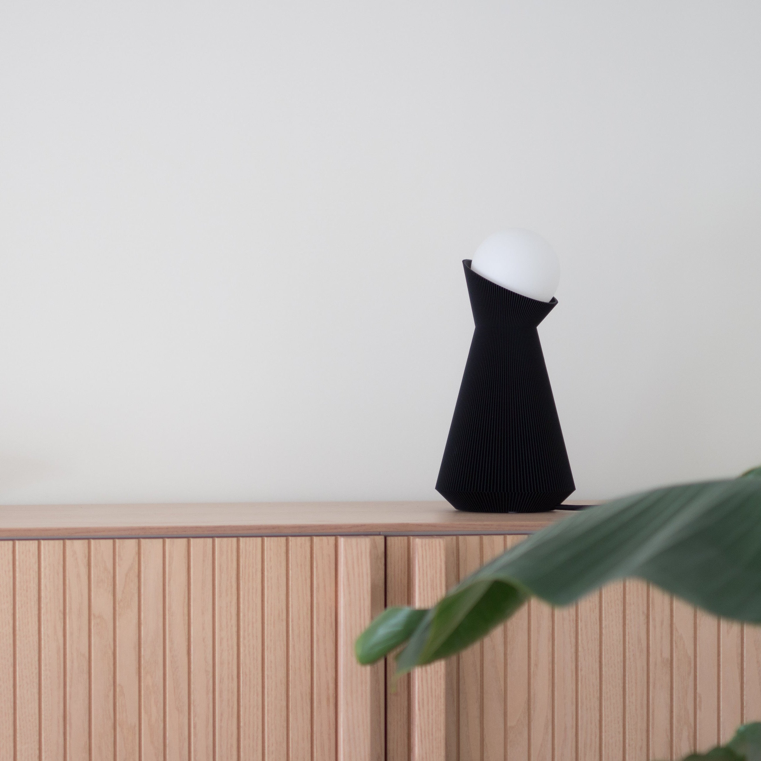 Black and white lamp on a wooden cupboard with a plant and a light background